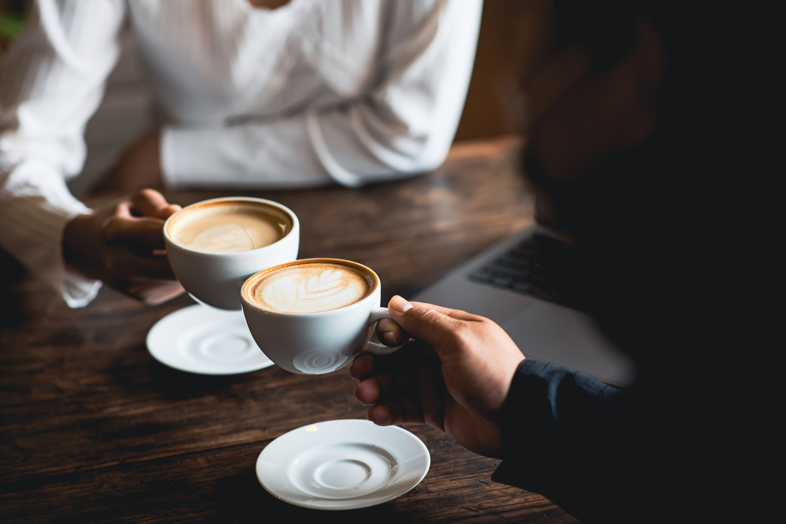 Close-up of a man and woman clinking a white coffee cup in a cof